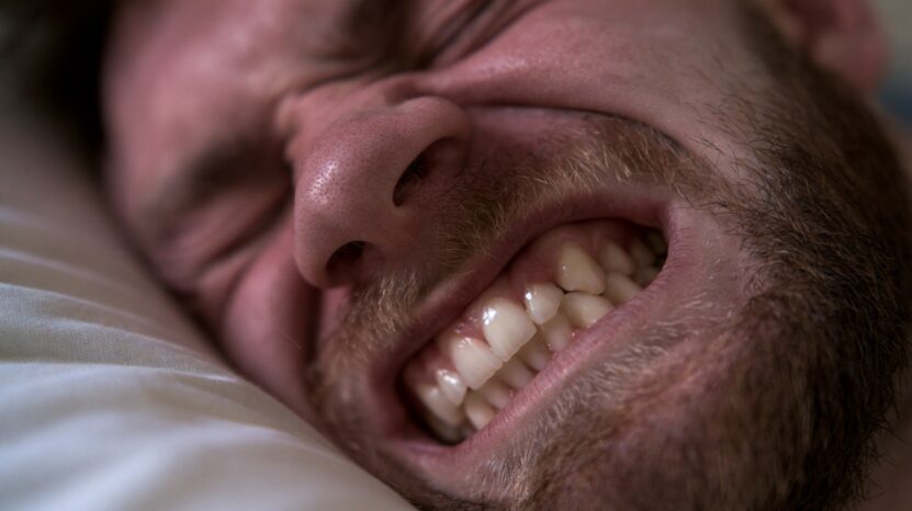 Close-up of a sleeping man clenching his teeth.